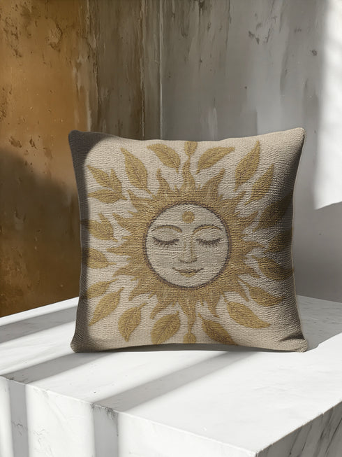 A square woven tapestry throw pillow in neutral earth tones of beige and gold. The pillow has a rich, textured surface from its jacquard weave. The design features a large, central celestial sun face with closed eyes, a serene smile, and a third eye symbol on its forehead. The sun's rays are stylized as intricate leaves, blending botanical and solar motifs. The pillow is made from a durable cotton and polyester blend, giving it a high-quality, artisanal feel.